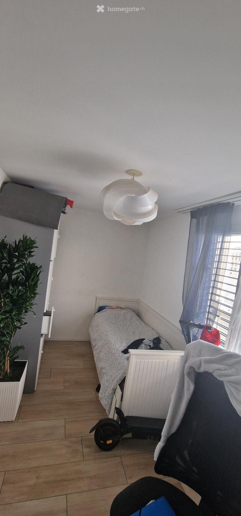 A small bedroom with a single bed, a chair, a modern lamp, a large window with curtains, and a potted plant. A scooter is placed near the bed.
