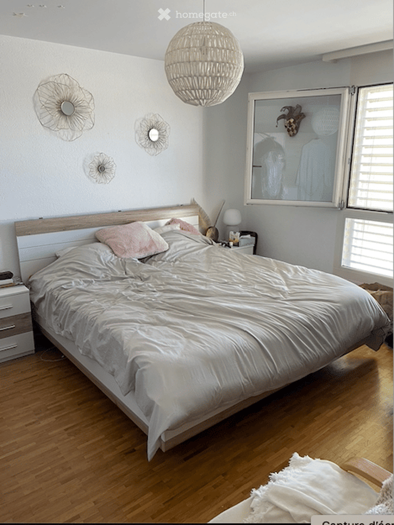 Modern bedroom with a large wooden bed, white bedding, pink pillows, a nightstand with a lamp, and decorative wall art.