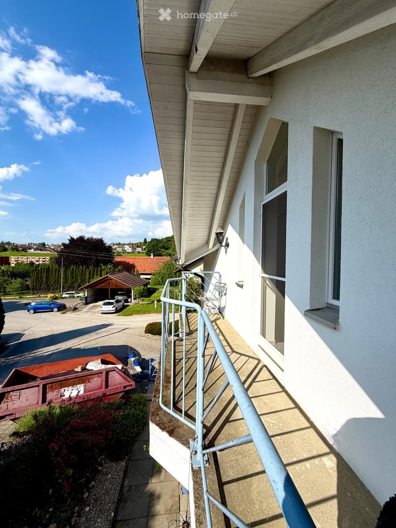 Balcony with metal railing, white folding chair, and a view of the street and surrounding buildings.