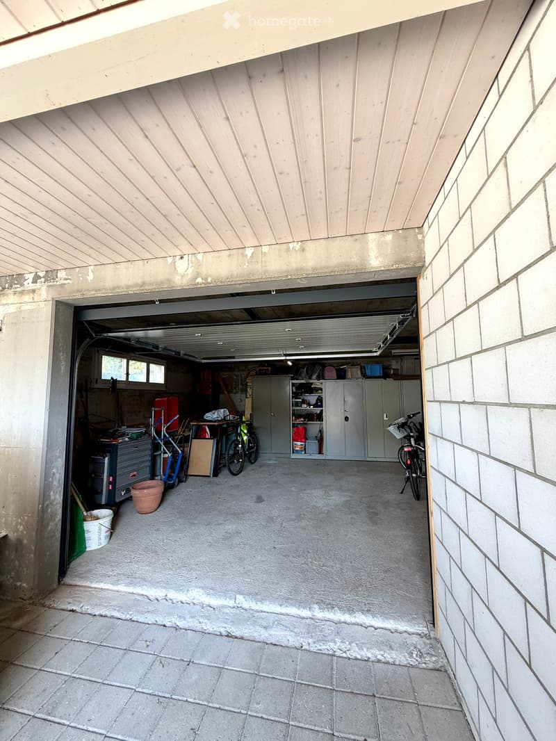 Garage with concrete floor, wooden ceiling, storage cabinets, bicycles, and various tools.