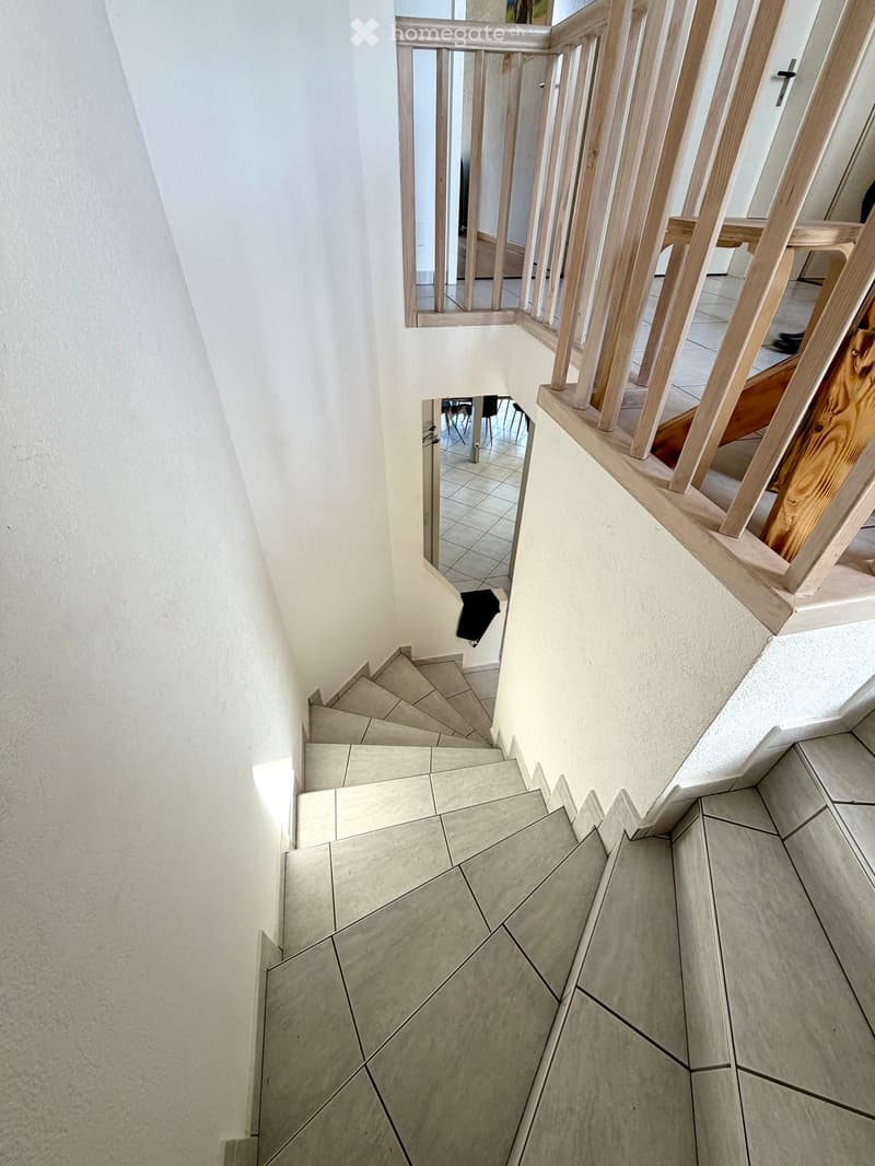 Spiral staircase with wooden handrails and tiled steps, leading to an upper level with visible room and furniture.