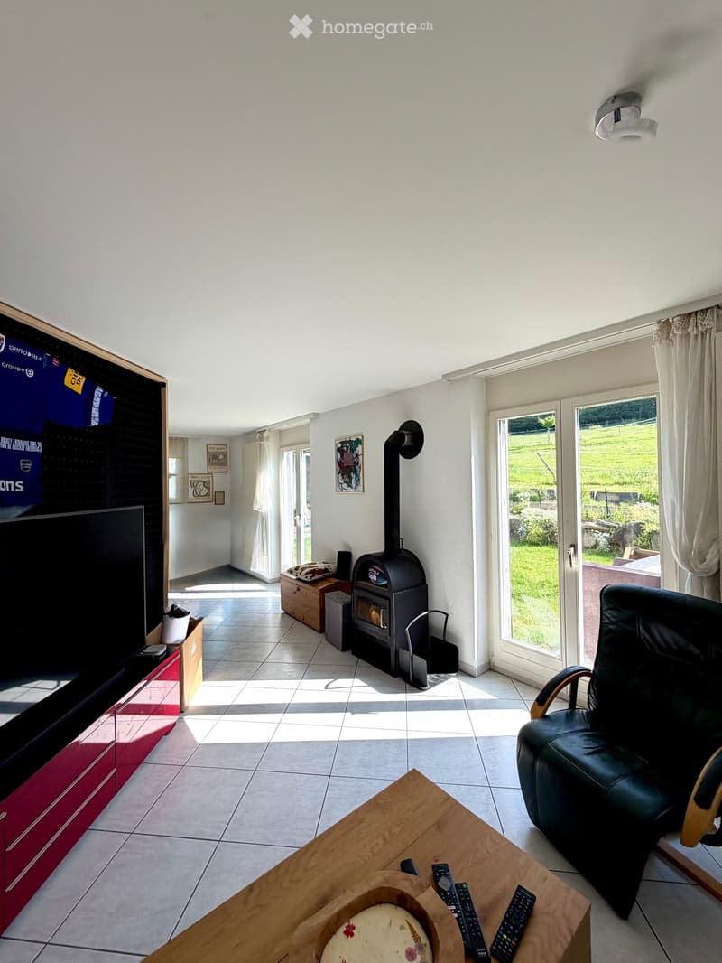Bright living room with tiled floor, large window, fireplace, sofa, coffee table, and TV.