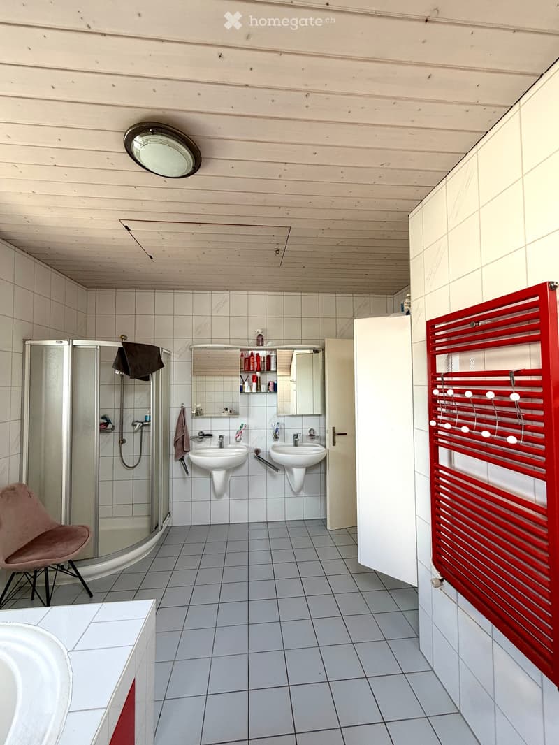 Modern bathroom with two sinks, a mirror cabinet, a red radiator, a shower, and a pink chair.