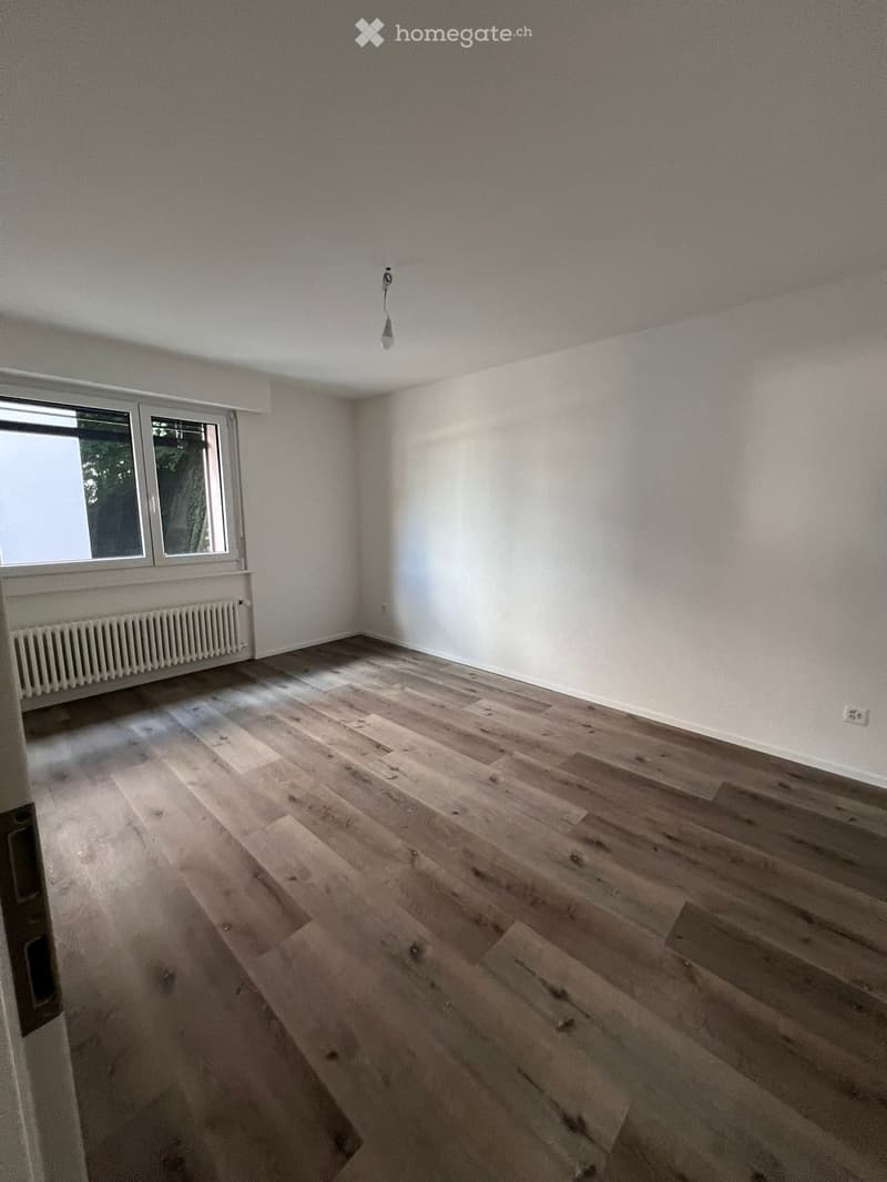 Empty room with wooden flooring, white walls, and a window with a radiator below it.