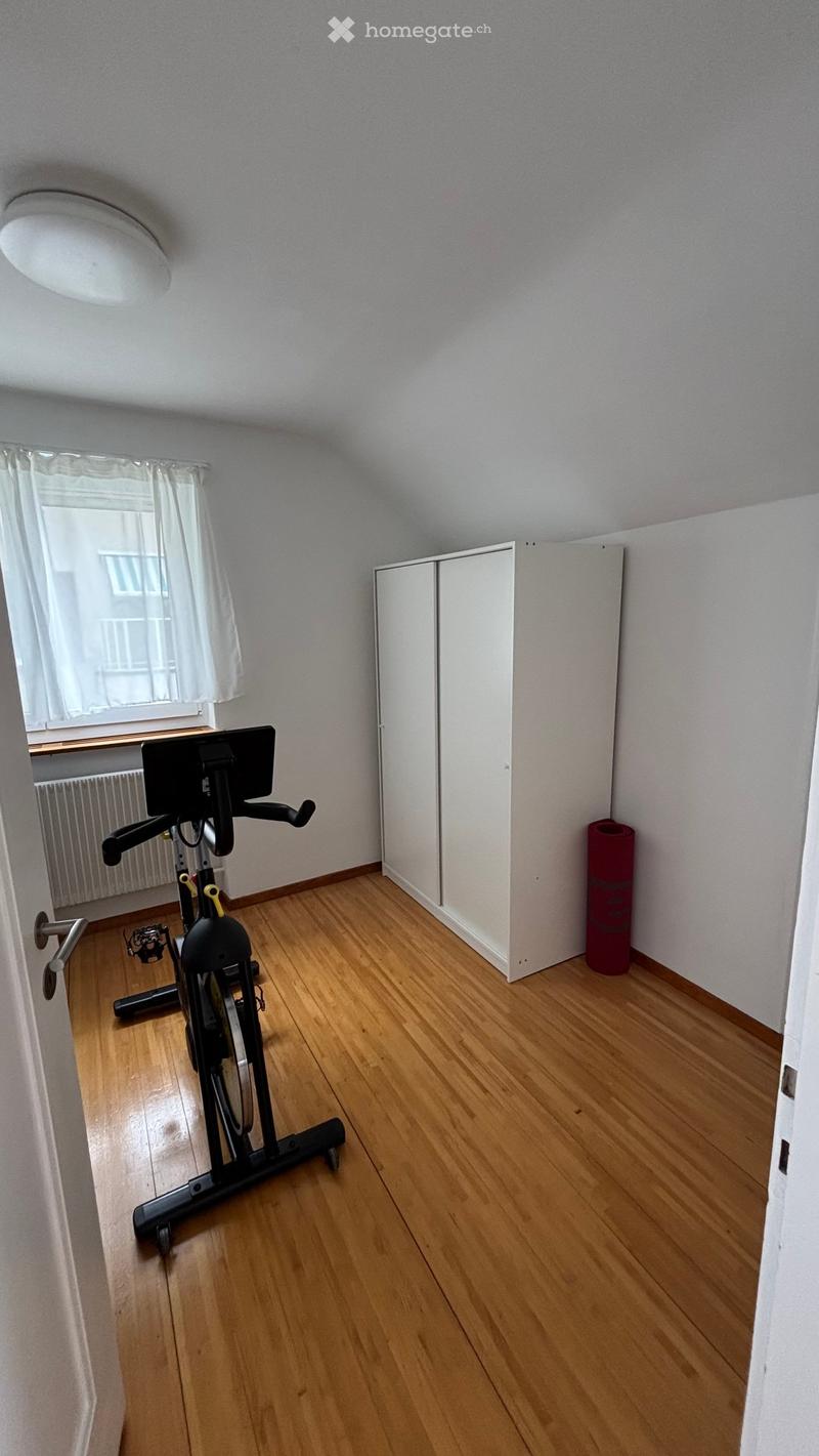 Exercise room with wooden flooring, an exercise bike, a white wardrobe, and a red yoga mat in the corner.
