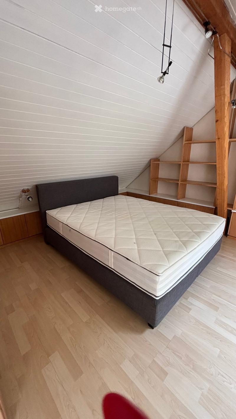 Spacious bedroom with wooden flooring, a large bed with a quilted mattress and dark headboard, and built-in wooden shelves on the wall.