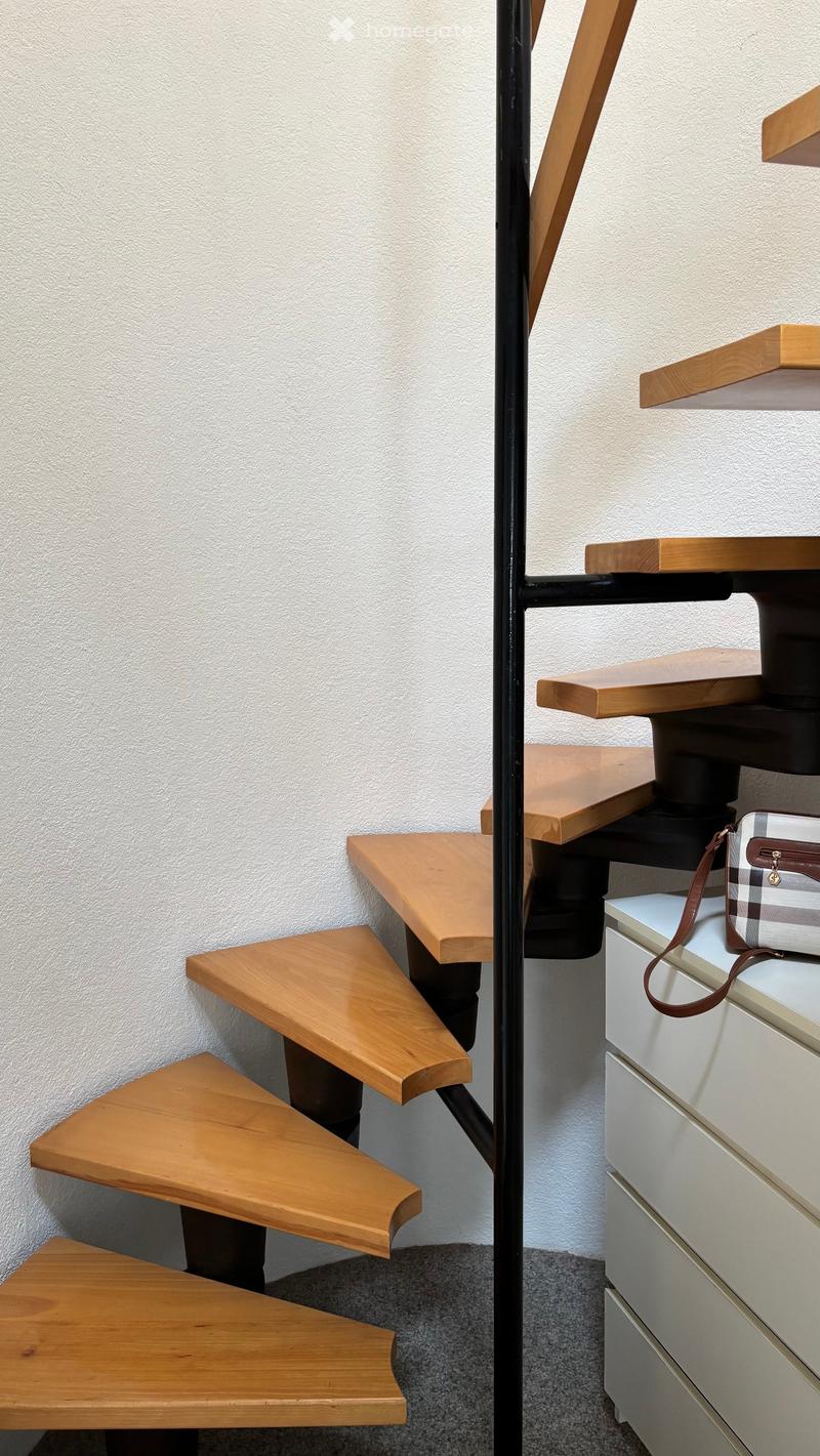 A modern staircase with wooden steps and a black metal railing, adjacent to a white cabinet with a handbag placed on top.