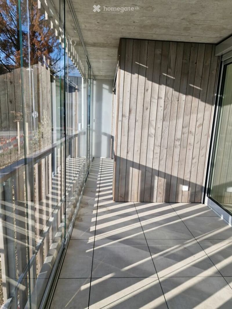 Modern balcony with glass railing, wooden panel wall, tiled floor, and natural light.