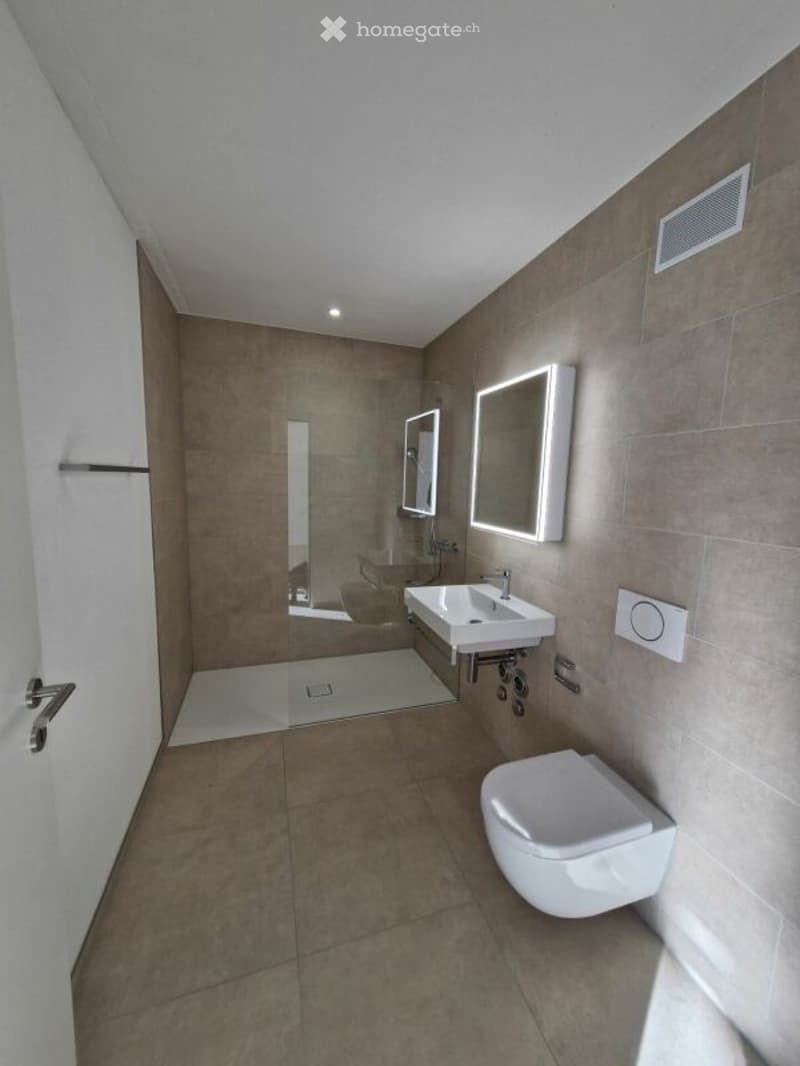 Modern bathroom with beige tiles, white fixtures, and illuminated mirrors.
