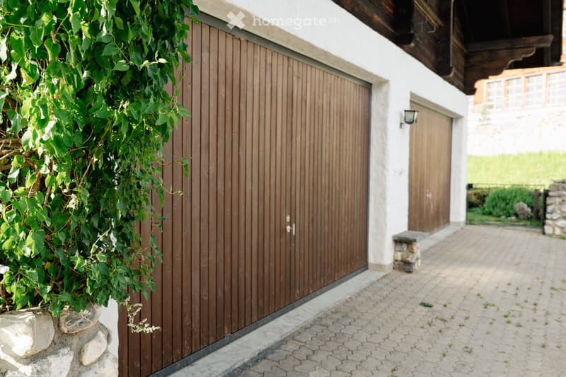 A modern house exterior with a wooden garage door, a small garden area, and a paved driveway.
