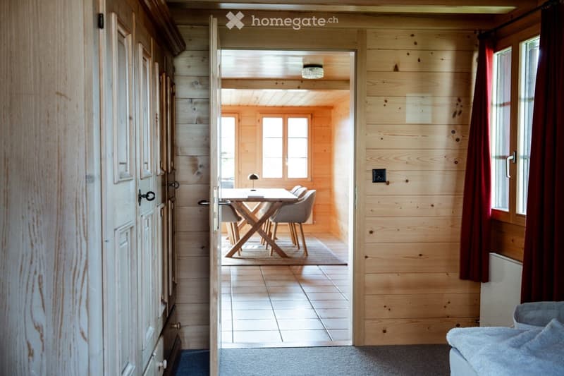 A cozy, wooden-paneled room with a dining table and chairs, a small lamp, and large windows letting in natural light.
