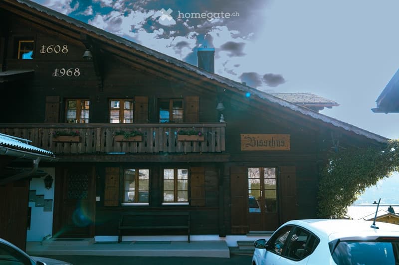 Traditional wooden chalet with a steep roof, large windows, and a balcony adorned with flower boxes. The building features a sign reading "Misselhus" and has a mix of dark wood and light-colored trim.