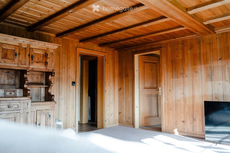A cozy wooden-paneled room with exposed wooden beams on the ceiling, featuring a large wooden cabinet and a television on a stand.