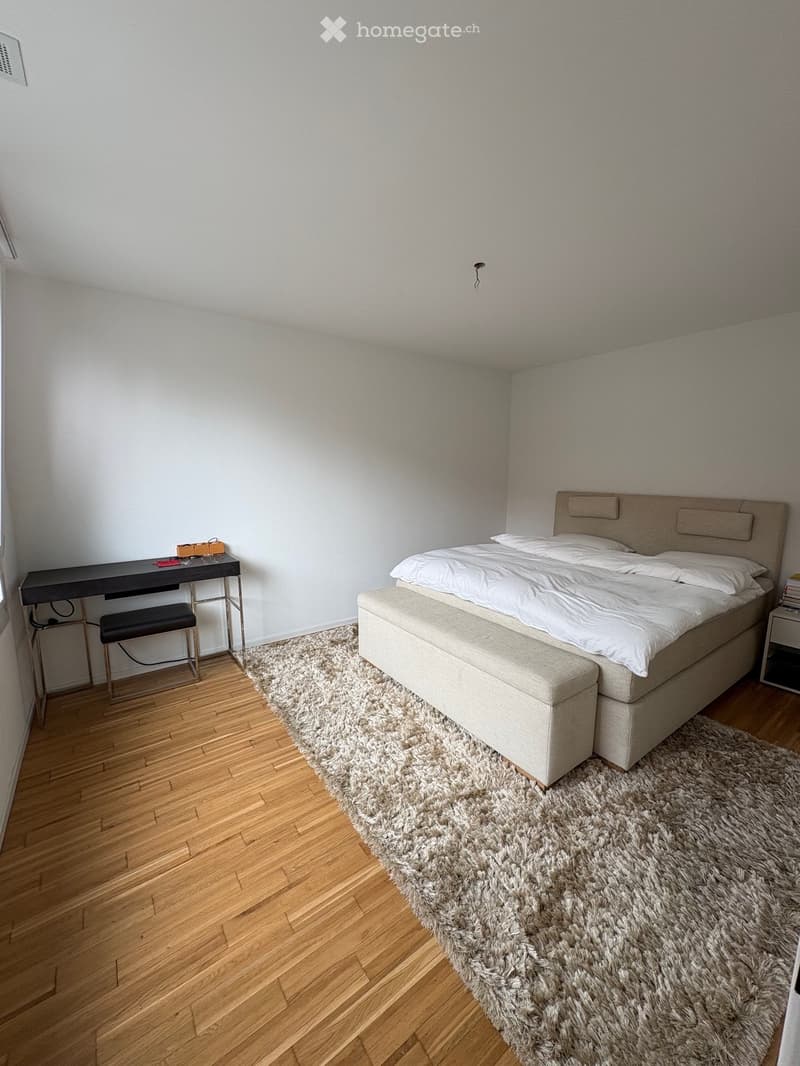 Modern bedroom with a large bed, nightstand, desk, and a fluffy rug on a wooden floor.