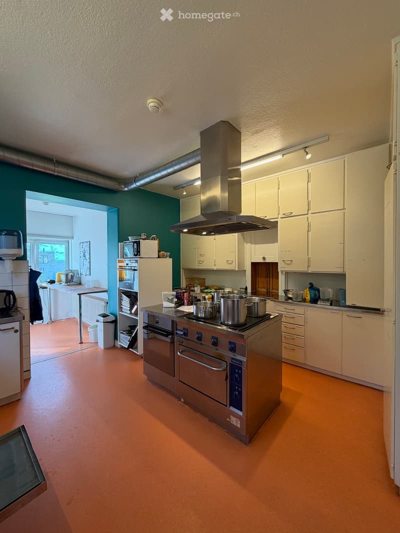 Commercial kitchen with stainless steel appliances, green wall, and orange floor.
