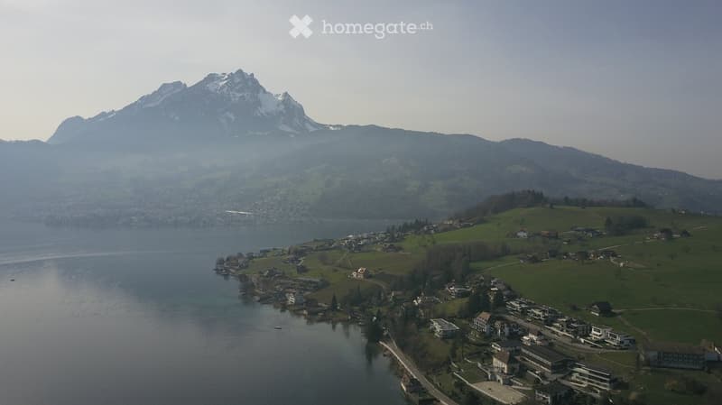 Aerial view of a serene landscape featuring a lake, a village, and a mountain range.