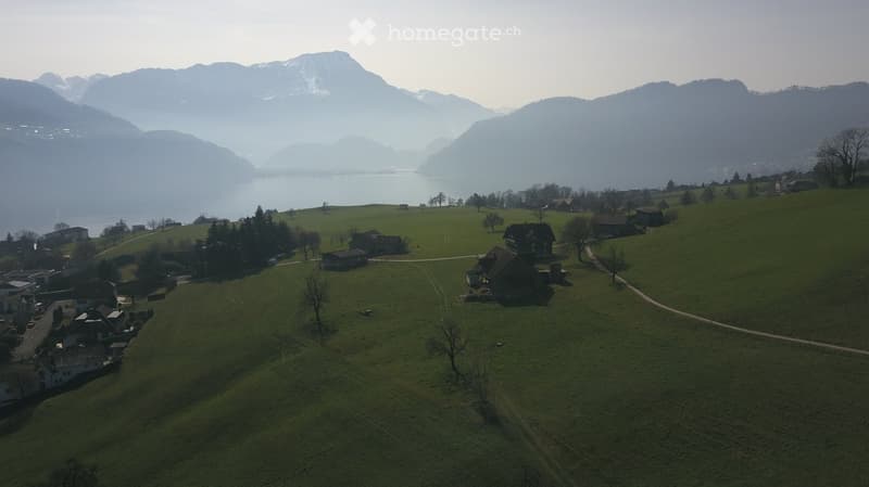 Aerial view of a serene countryside with a lake, mountains, and several houses scattered across the landscape.