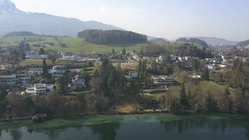 Aerial view of a hillside community with modern buildings, surrounded by greenery and mountains.