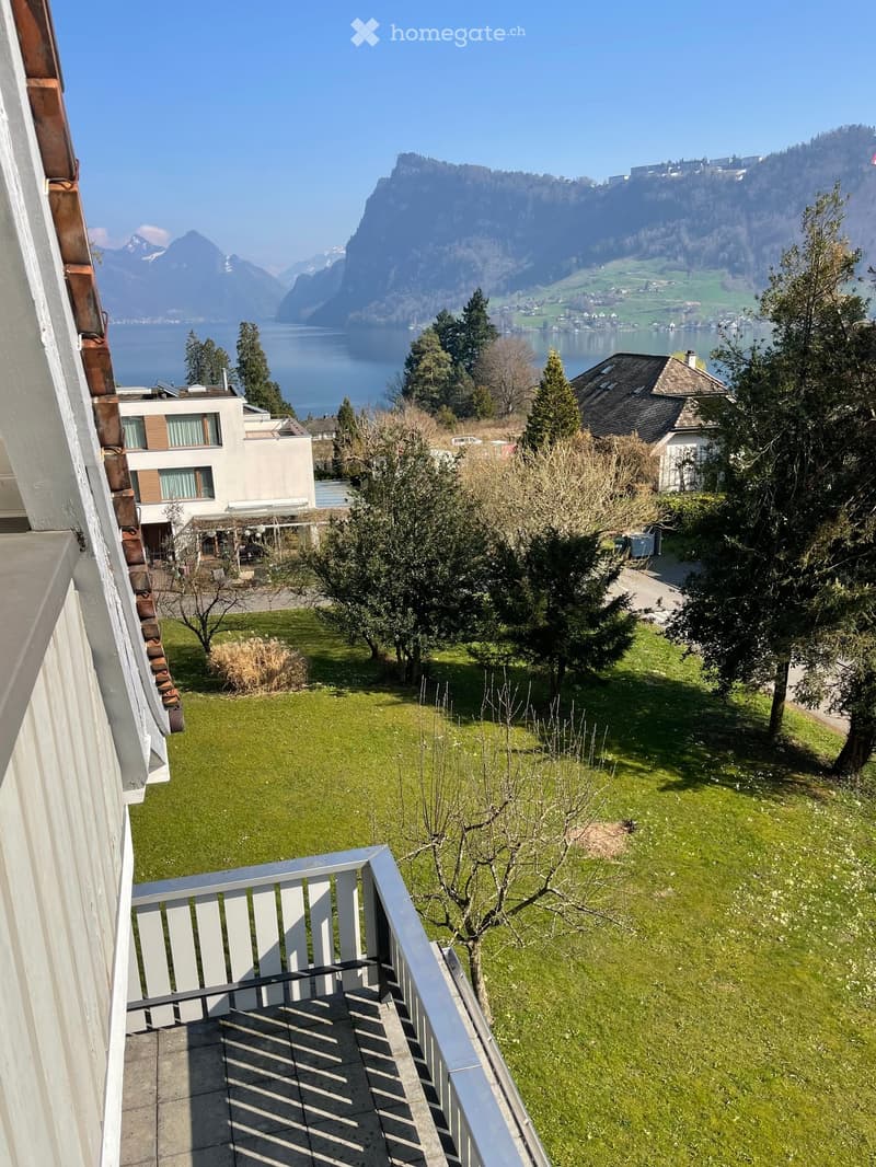 A balcony with a metal railing overlooking a grassy area with trees and a lake in the distance.