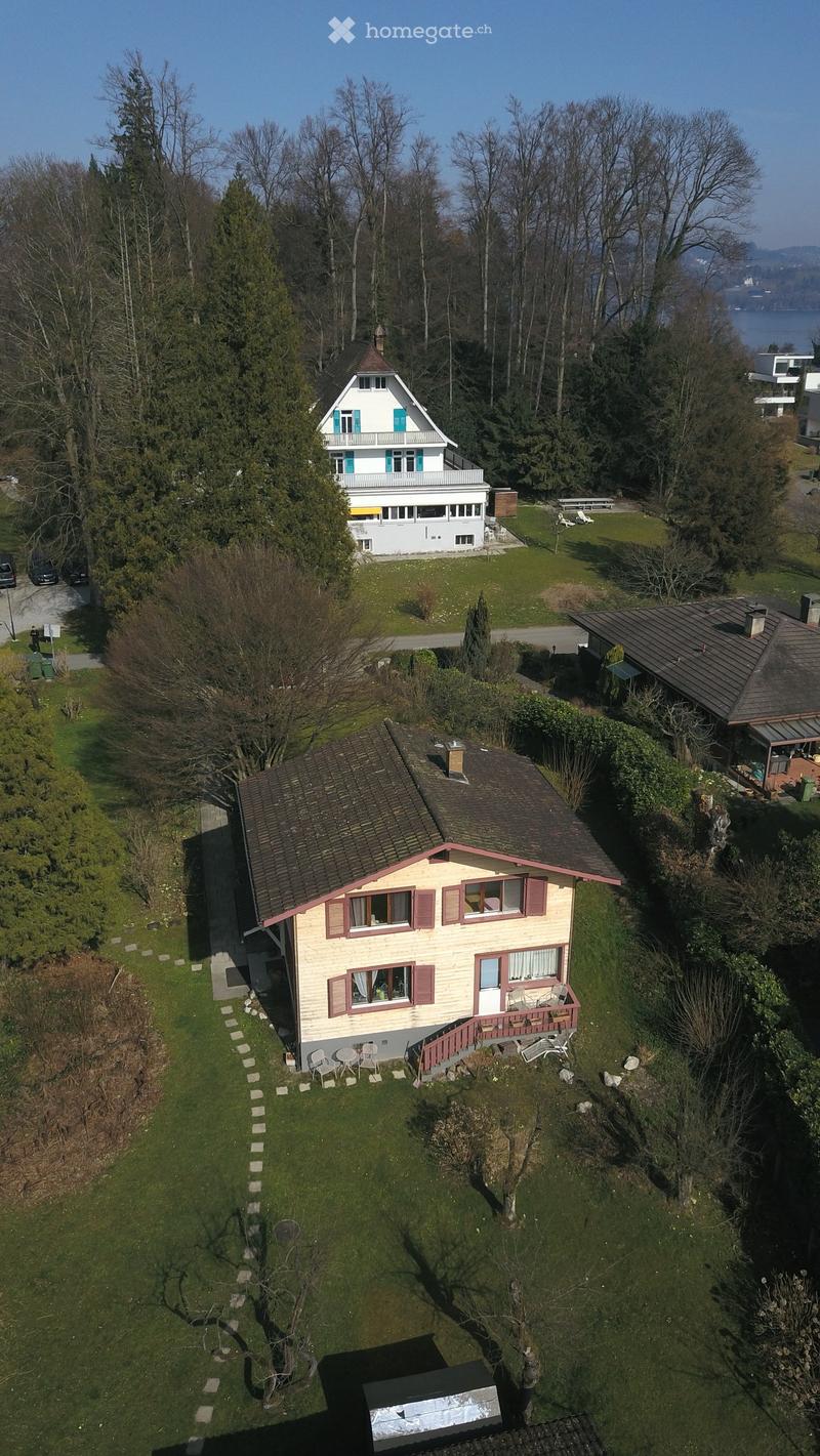 Aerial view of a house with a brown roof and a garden, surrounded by trees and grass.