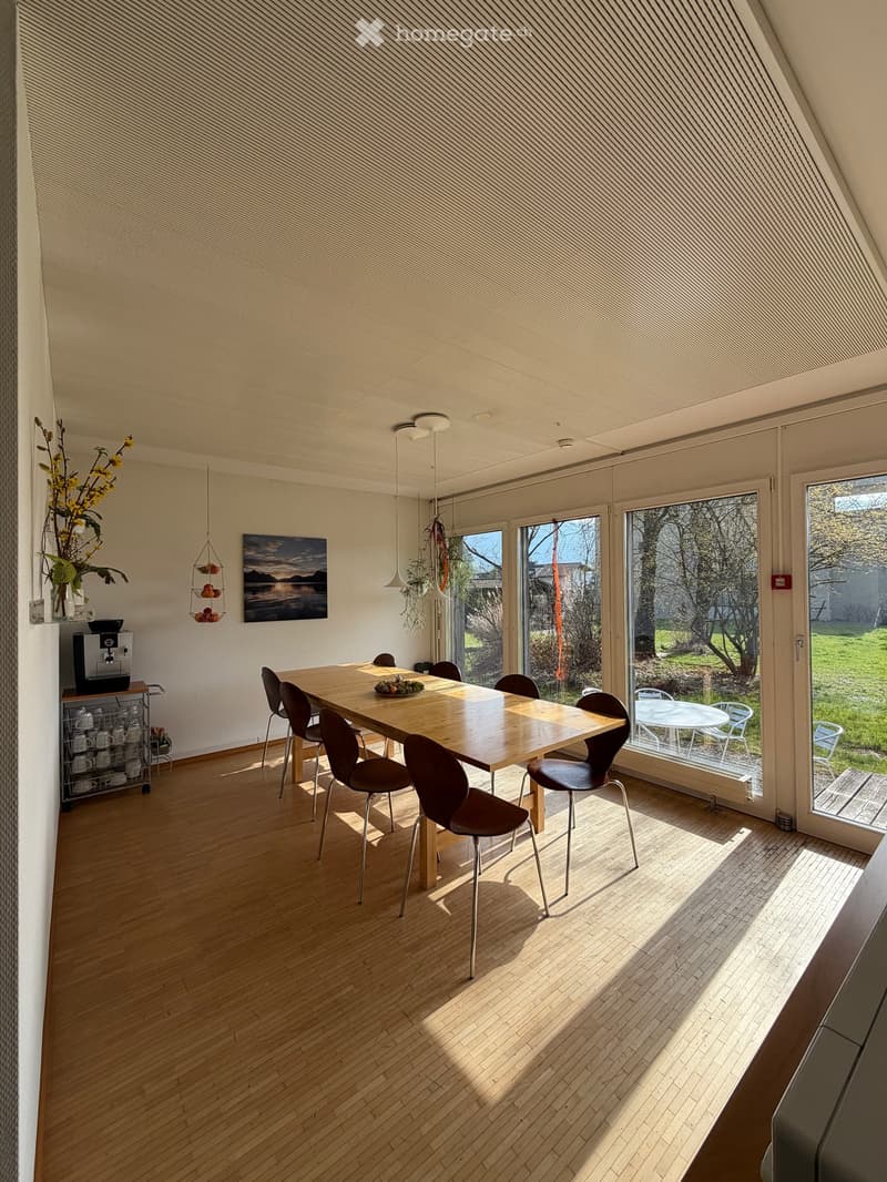 Spacious room with wooden floor, large dining table, chairs, coffee machine, flowers, painting, lamps, and outdoor table and chairs.