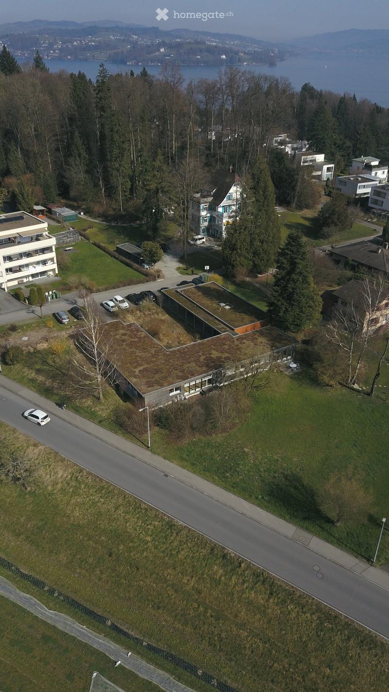 Aerial view of a residential building complex with several houses, a road, and a lake in the background.