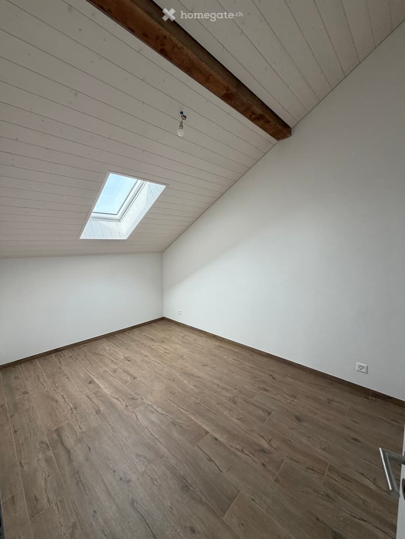 Empty room with wooden flooring, white walls, and a skylight window in the ceiling.