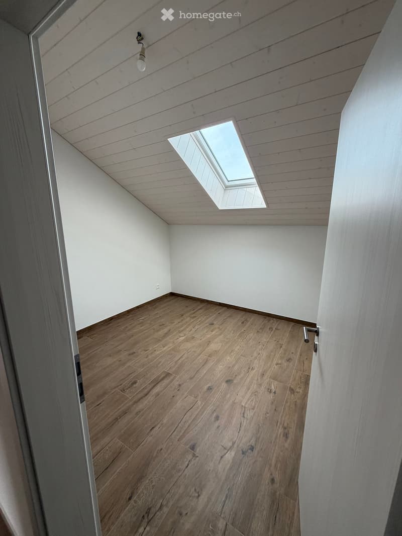 Empty room with wooden flooring, white walls, and a skylight window in the ceiling.