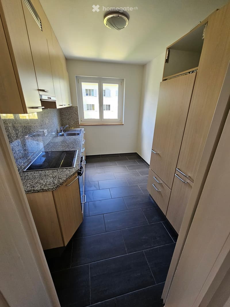 Modern kitchen with dark tiled floor, granite countertops, built-in cabinets, and a window overlooking a building.