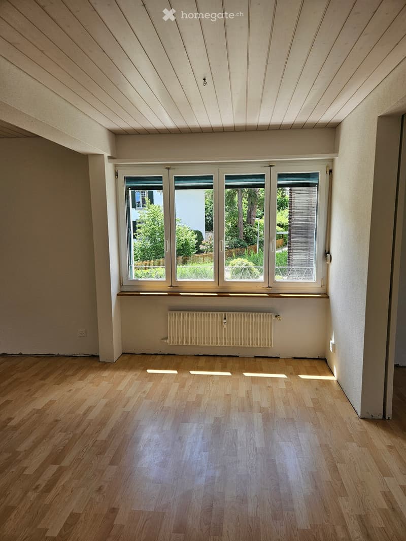 Empty room with wooden flooring, large windows, radiator, and exposed wooden ceiling beams.