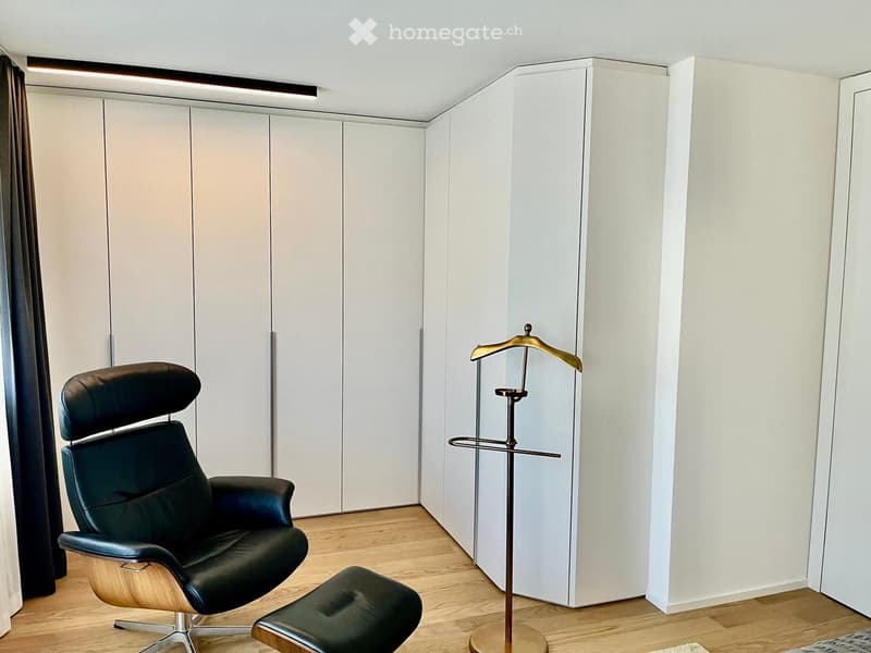 Modern minimalist bedroom, high ceiling, built-in wardrobes, a black leather chair, wooden floor, and an air coat rack.