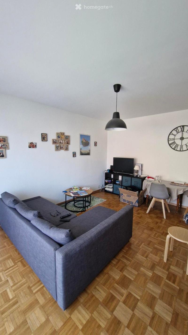 Living room with wooden flooring, grey sofa, coffee table, dining table, chairs, television, and decorative wall art.