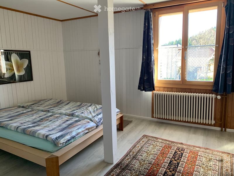 Cozy bedroom with two single beds, a radiator, a window with curtains, a picture frame on the wall, and a small stool near the beds.