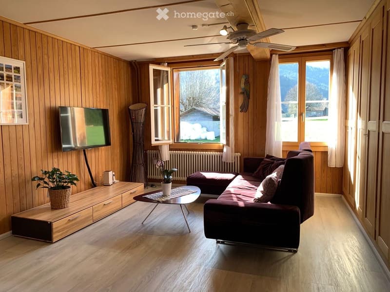 Living room with wooden walls and floor, large windows, sofa, coffee table, TV, and plants.