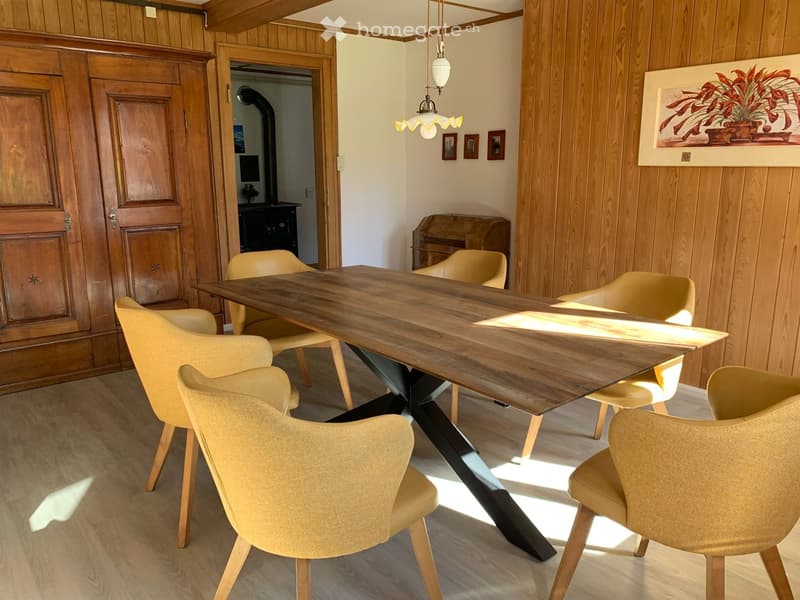 Dining room with a long wooden table surrounded by six light yellow chairs, wooden cabinet, and artwork on the wall.
