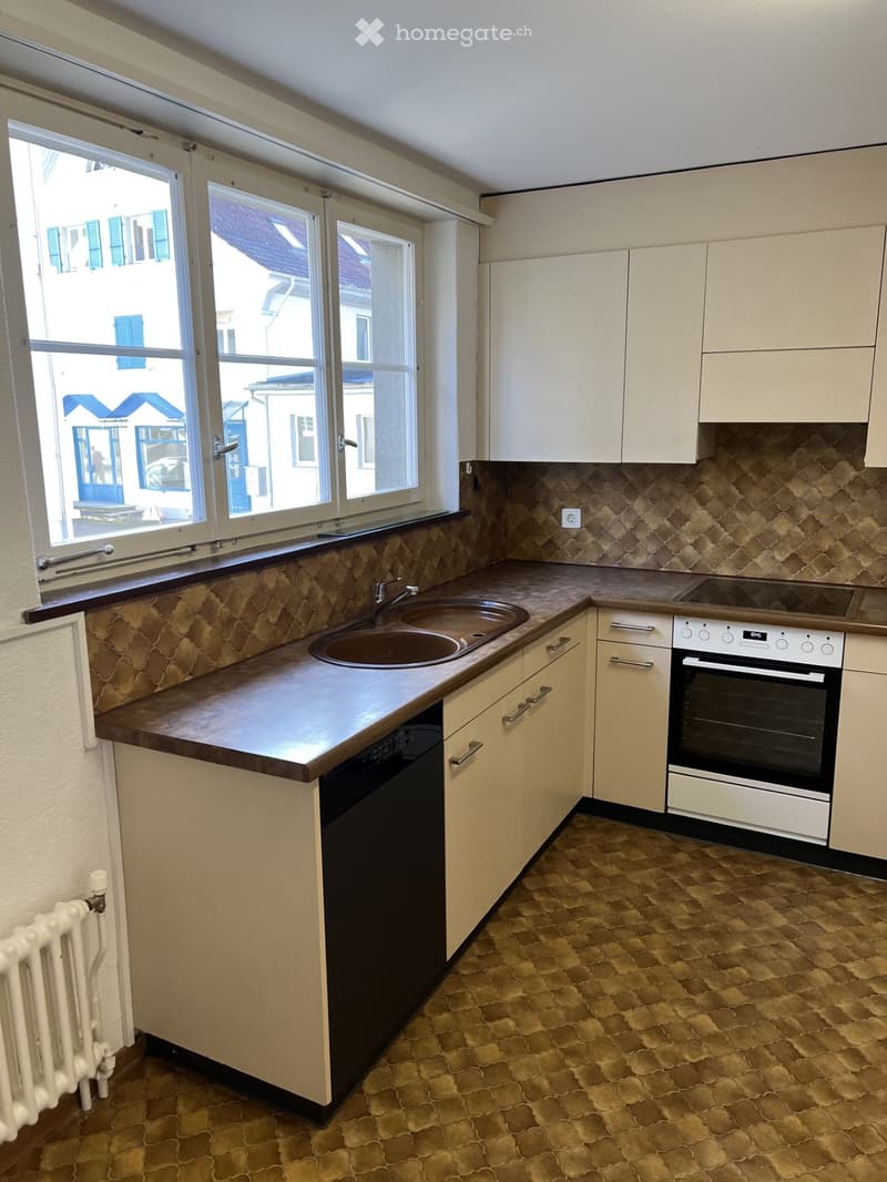 Modern kitchen with light-colored cabinets, a double sink, an oven, and a dishwasher. The countertops are made of wood, and the backsplash features a patterned tile design.
