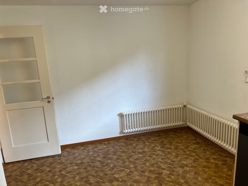 Empty room with white walls, brown tiled floor, white radiator, and a door with glass panels.