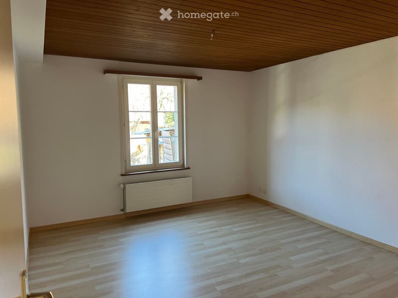 Empty room with wooden flooring, white walls, and a window with a radiator below it.