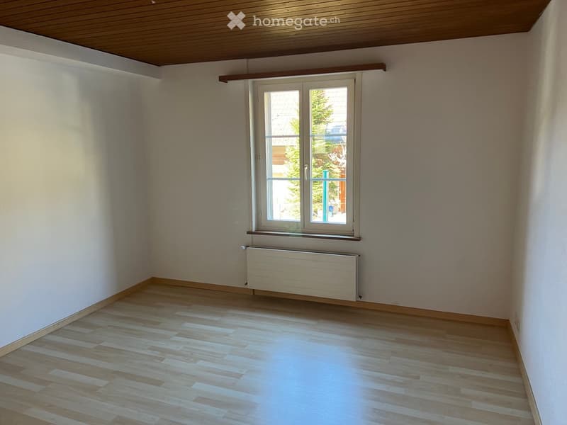 Empty room with wooden flooring, white walls, and a window with a radiator below it.