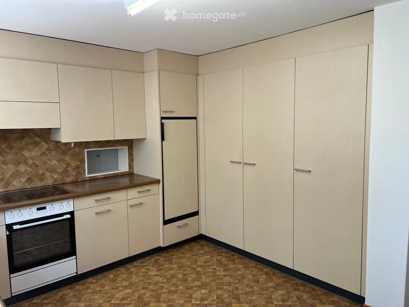 Modern kitchen with light-colored cabinets, a built-in oven, and a refrigerator. The countertop is made of wood, and the backsplash features a textured, patterned tile design.