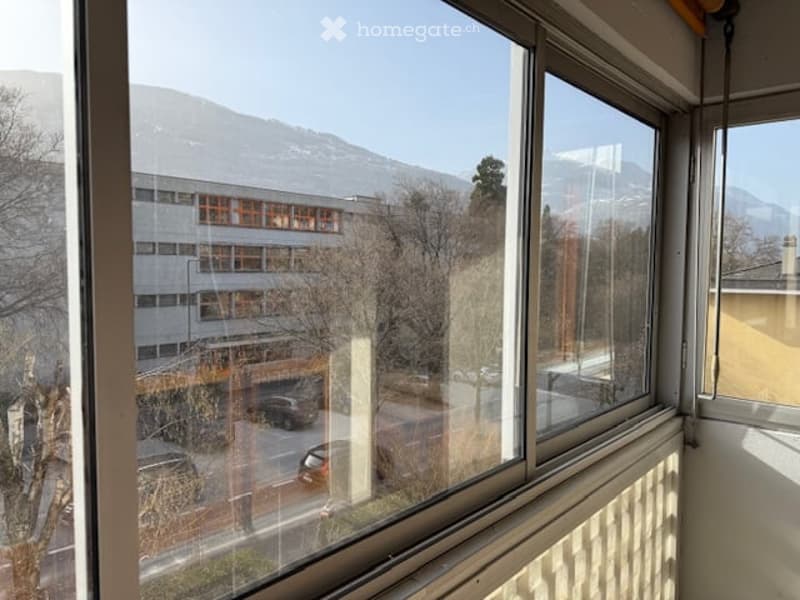 Empty room with large windows offering a scenic mountain view and a view of a building and street below.