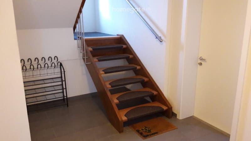 {"visible_features": ["Raised ground floor"],    "type": "Stairs",    "description": "wooden stairs with carpeted steps, stainless steel handrail, white door on the right, tiled floor, small doormat, metal stand with hangers",    "localized_description