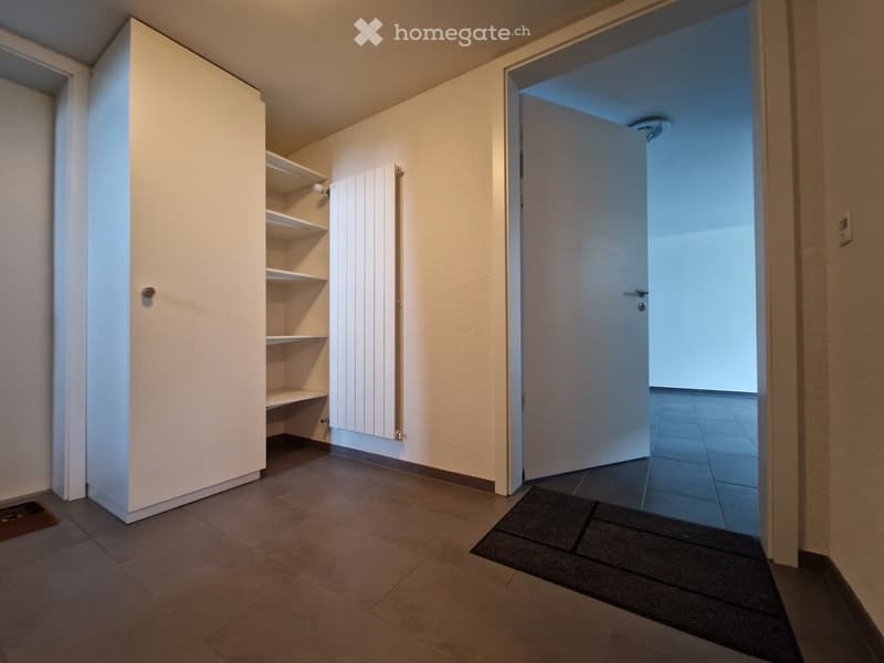 {"type": "Room",    "description": "A room with white walls, tiled floor, and built-in shelves. There is a white wardrobe with silver handles, a radiator on the wall, and a white door that is open, revealing a hallway.",    "localized_descriptions":