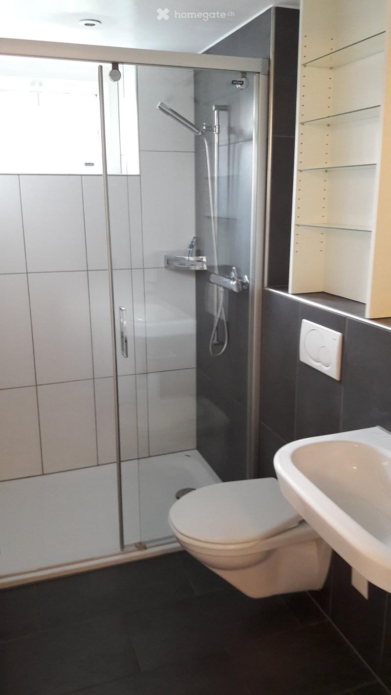 modern bathroom with white tiles, glass enclosed shower, white toilet, and a white sink