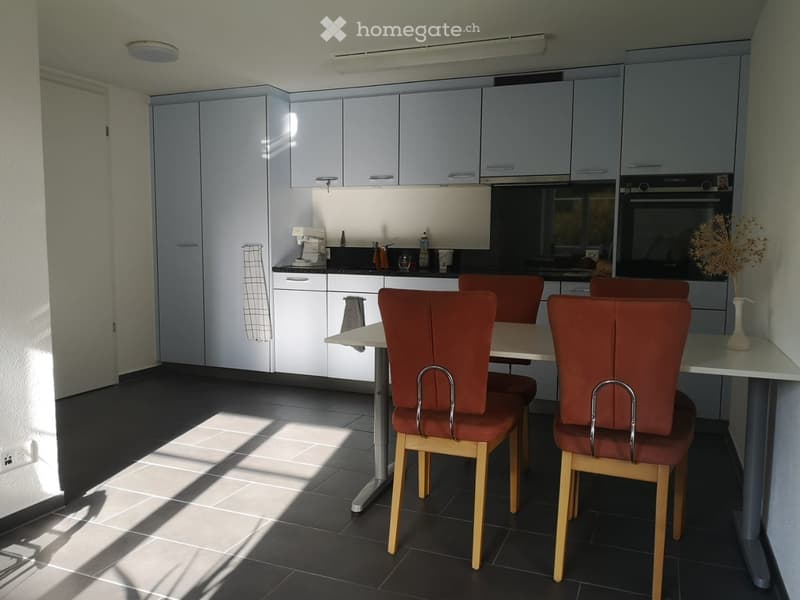 Modern kitchen with white cabinets, dark tile flooring, and a dining table with chairs.