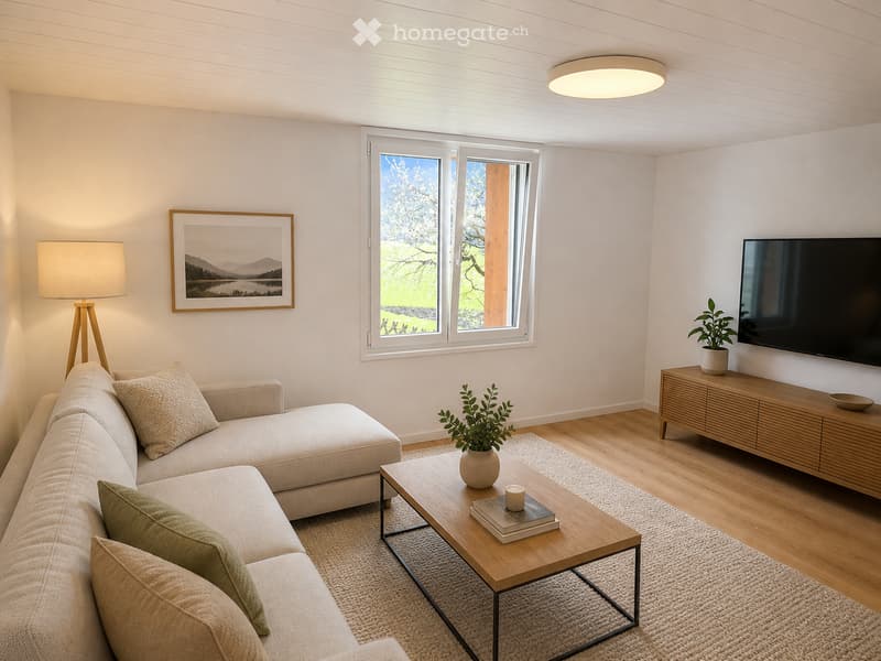 Modern living room with a light-colored sectional sofa, wooden coffee table, floor lamp, wall-mounted TV, and large windows offering a view of greenery.