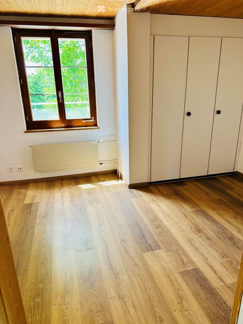 Empty room with wooden flooring, white walls, built-in closet, window with wooden frame, radiator, and electrical outlets.