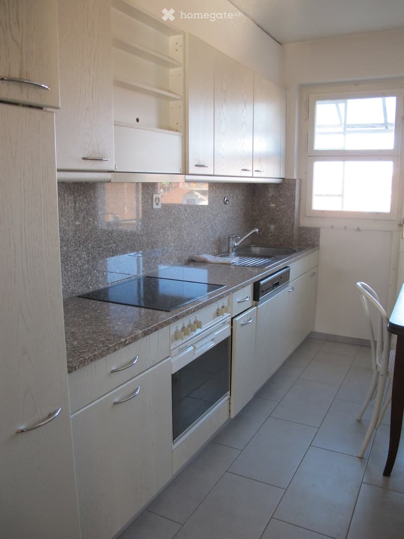 Modern kitchen with white cabinets, granite countertops, built-in oven, dishwasher, and sink.