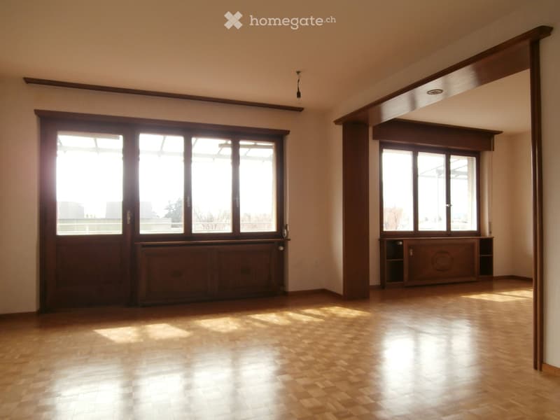 Empty room with wooden flooring, large windows, and built-in wooden cabinetry.