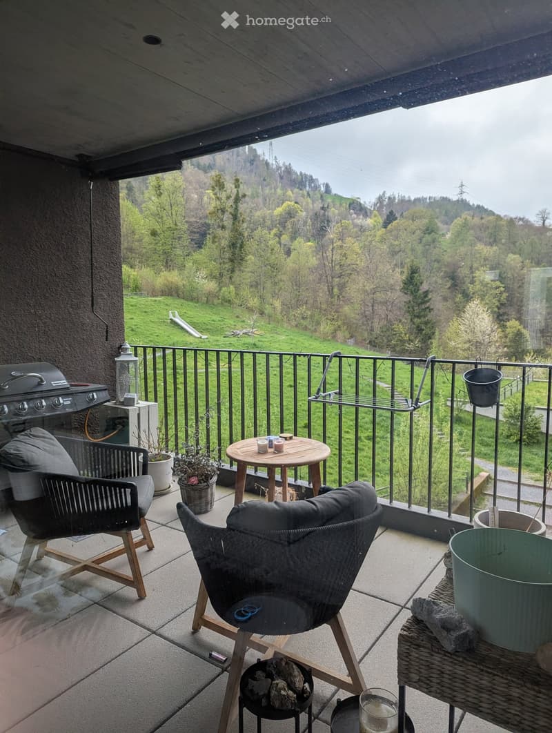 Balcony with a scenic view, featuring a round wooden table, two chairs, a grill, and decorative items.